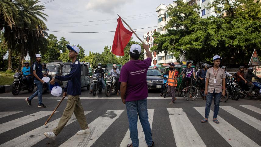 Student managing traffic at Bijoy Sarani and waving a red flag signaling them to go forward. 