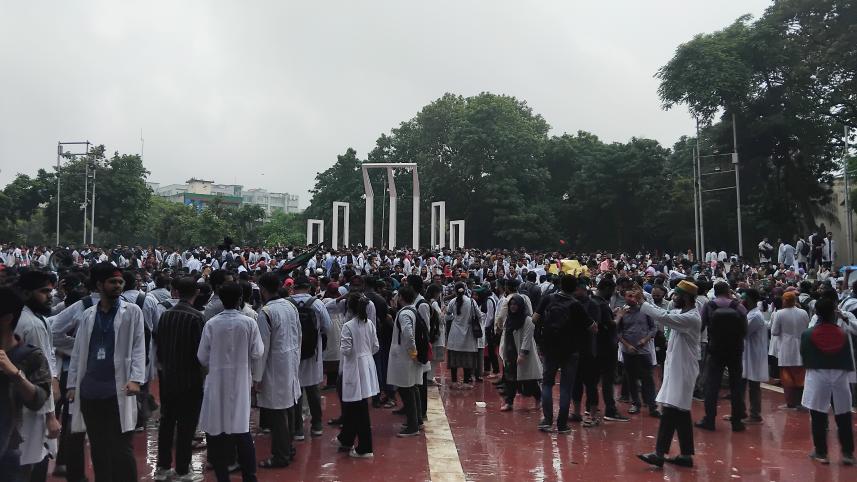A large group of students who are wearing lab coats and standing in front of the Shaheed Minar  