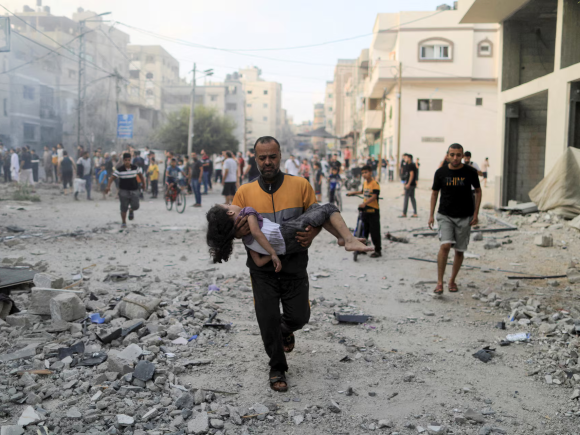 A Palestinian man carries a wounded girl at the site of Israeli strikes.png