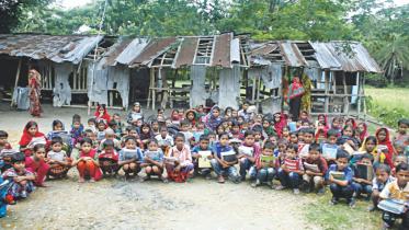 Children sitting with books in front of a damaged school house.