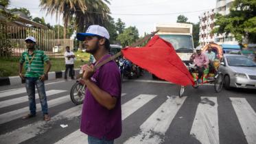 A student managing the traffic at Bijoy Sarani while resting a red flag on his shoulder.  
